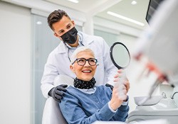 Woman with black glasses smiling at reflection in handheld mirror