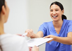 Dental team member smiling and offering paperwork to root canal patient