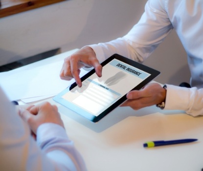 Dentist and ental patient looking at dental insurance forms on tablet computer