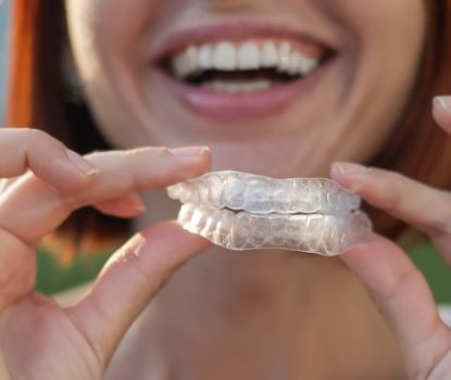 Closeup of smiling dental patient holding nightguards for bruxism