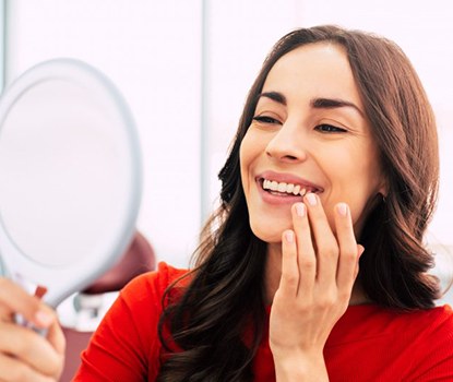 Woman smiling as she looks at a small mirror