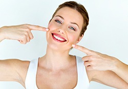 Woman in white tank top pointing to her smile with two fingers