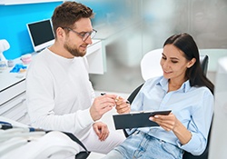 Woman wearing denim sitting in dental chair filling out forms on clipboard