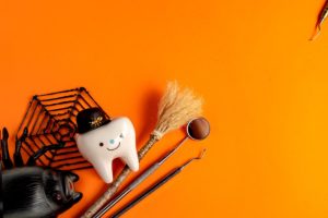 Model tooth, dental instruments, and Halloween toys on an orange background