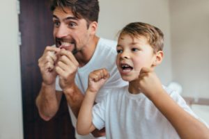 Man and boy in white t-shirts flossing their teeth together in the bathroom