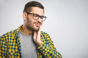 Man in plaid shirt with glasses holding side of his face in pain.
